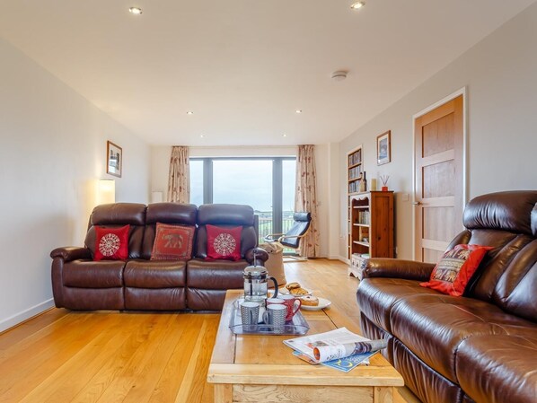 A living room with two leather sofas, a coffee table with items, and a bookshelf. - 5 Bed in Bideford (oc-76546) (Hartland)