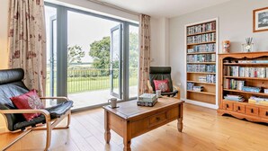 A living room with a sofa, a coffee table, a bookshelf, and a view through a large sliding glass door. - 5 Bed in Bideford (oc-76546) (Hartland)
