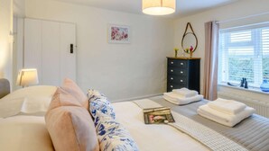 Une chambre à coucher comprenant un lit, une table de chevet, une commode, une fenêtre et un luminaire suspendu.