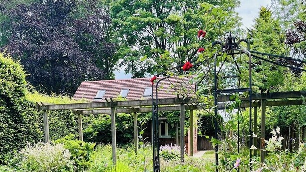 A garden with a wooden pergola, a house with a red roof, and various plants. - Countryside Garden Loft near Lymm (Warrington)