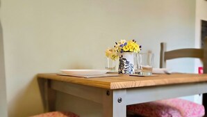 A dining table with a vase of flowers, a chair with a floral cushion, and a wall-mounted picture. - Countryside Garden Loft near Lymm (Warrington)