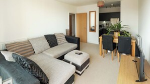 A living room with a sofa, ottoman, and a dining area with a table and chairs. - Modern Flat with Balcony near Hackney Wick (London)
