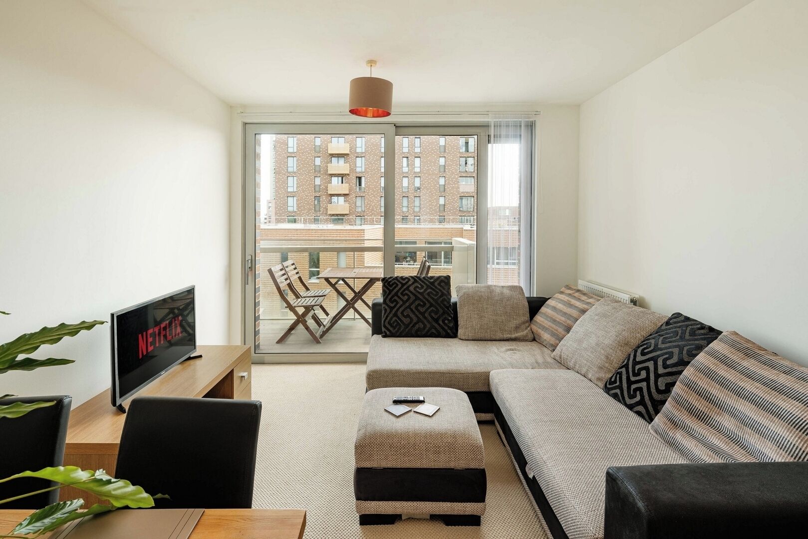 Una sala de estar moderna con sofá, reposapiés, mesa de centro, televisor y un balcón con vistas a edificios.