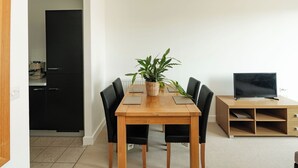 A dining area with a wooden table, black chairs, a potted plant, and a television on a wooden stand. - Modern Flat with Balcony near Hackney Wick (London)