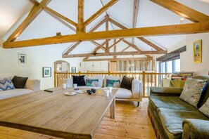 Ein geräumiges Zimmer mit hohen Decken, Holzbalken, einem großen Holztisch und zwei Sofas.