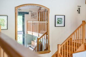Eine Treppe mit hölzernen Geländern führt zu einer erhöhten Ebene mit einem Klavier und gerahmten Kunstwerken an den Wänden.