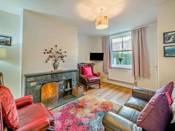 Una sala de estar con chimenea, sofás de cuero, una alfombra colorida y un televisor.