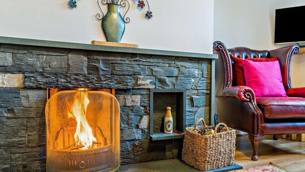 A stone fireplace with a fire, a woven basket, a leather armchair, and a colorful rug. - 2 Bed in Keswick (oc-95741) (Keswick)