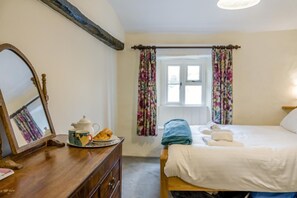 Ein Schlafzimmer mit einem Holzk dresser, einem Bett mit weißen Leinen und einem Fenster mit Blumen Vorhängen.