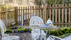 Ein Garten mit Tisch und Stühlen, einem Holzzaun und viel Grün.
