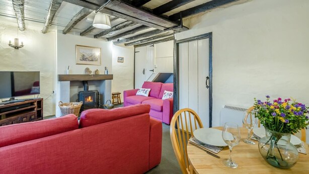 Ein gemütliches Wohnzimmer mit Kamin, roten Sofas, einem Esstisch mit Stühlen und einem Fernseher.