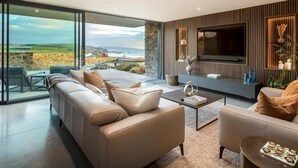 Ein modernes Wohnzimmer mit großem Fernseher, bequemen Sitzgelegenheiten und Blick auf den Ozean.