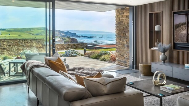 Ein modernes Wohnzimmer mit einem großen Glasfenster, das auf einen Balkon mit Blick auf eine Küstenlandschaft führt.