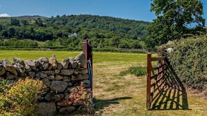 A stone wall with a gate, a grassy field, and a hill in the background. - 3 Bed in Conwy (oc-83154) (Rowen)