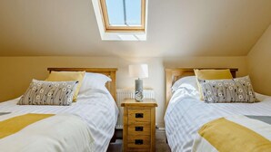 A bedroom with two beds, a skylight, bedside tables with lamps, and a radiator. - 3 Bed in Conwy (oc-83154) (Rowen)