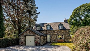 A stone house with a gravel driveway, a small garage, and a lawn. - 3 Bed in Conwy (oc-83154) (Rowen)