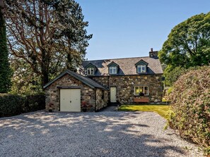 A stone house with a gravel driveway, a small garage, and a lawn. - 3 Bed in Conwy (oc-83154) (Rowen)