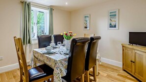A dining area with a table set for four, chairs, a cabinet, and a television. - 3 Bed in Conwy (oc-83154) (Rowen)
