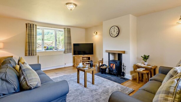 A cozy living room with a fireplace, a television, and a clock on the wall. - 3 Bed in Conwy (oc-83154) (Rowen)