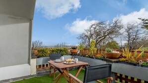 En terrasse med et bord og stole, udsigt over landskabet og krukker med planter.