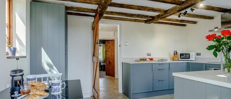 A kitchen with a wooden ceiling, a dining area with a table set for breakfast, and a view into another room.