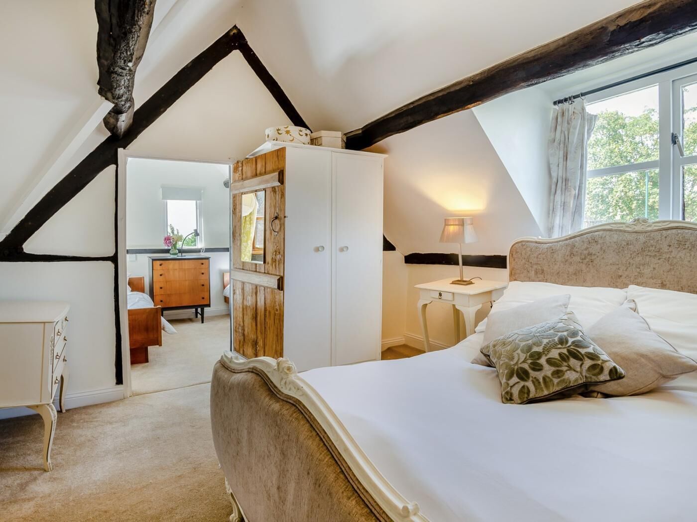 Une chambre avec un plafond en pente, un lit avec une tête de lit, une table de chevet, une commode et un miroir.