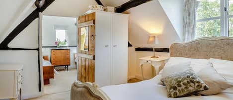 Une chambre avec un plafond en pente, un lit avec une tête de lit, une table de chevet, une commode et un miroir.