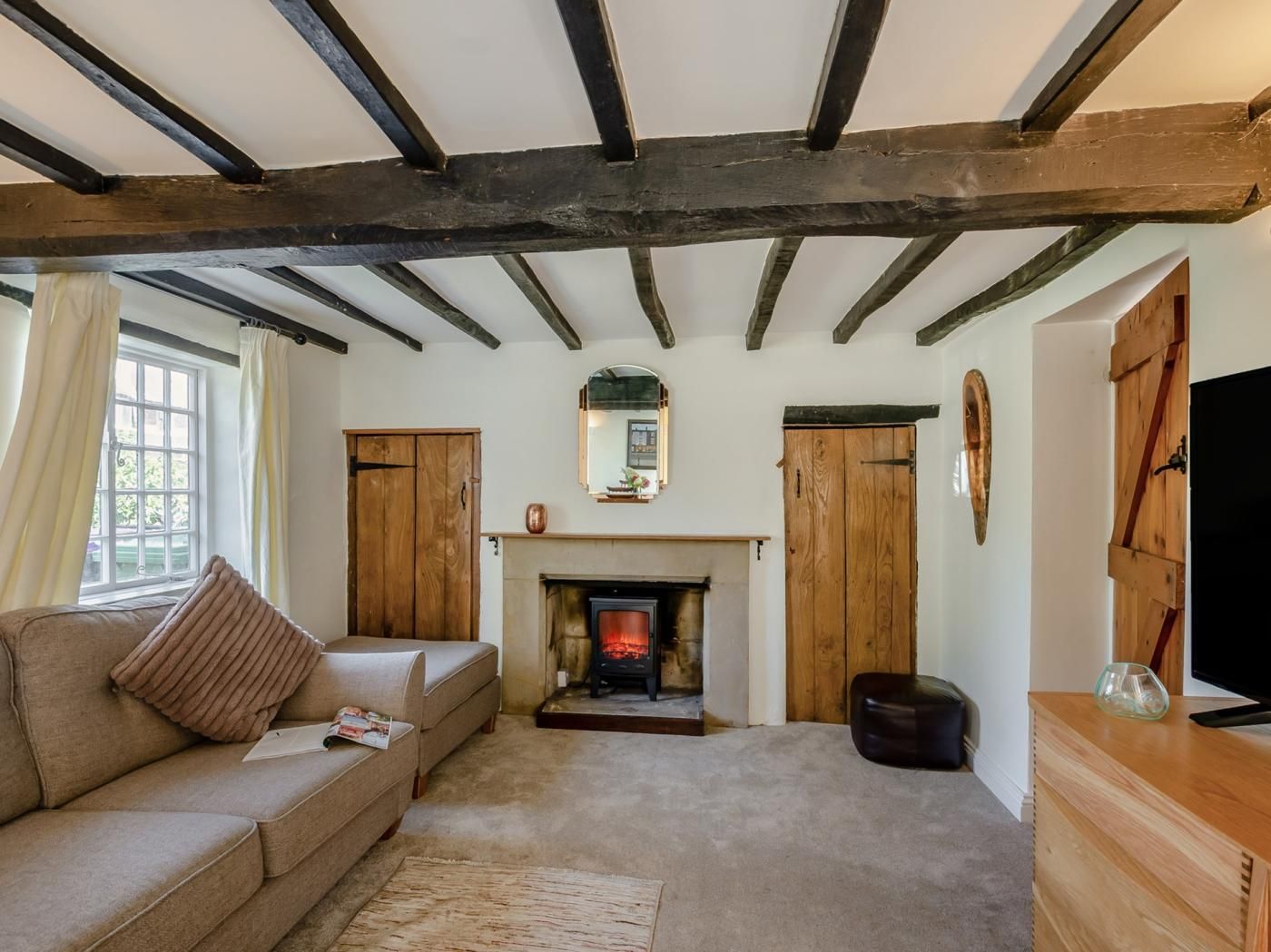 Una sala de estar acogedora con vigas de madera a la vista, una chimenea, un sofá y un televisor.