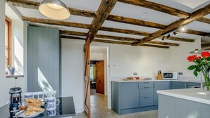 Una cocina con techo de madera, un comedor con mesa lista para el desayuno y vista a otra habitación.