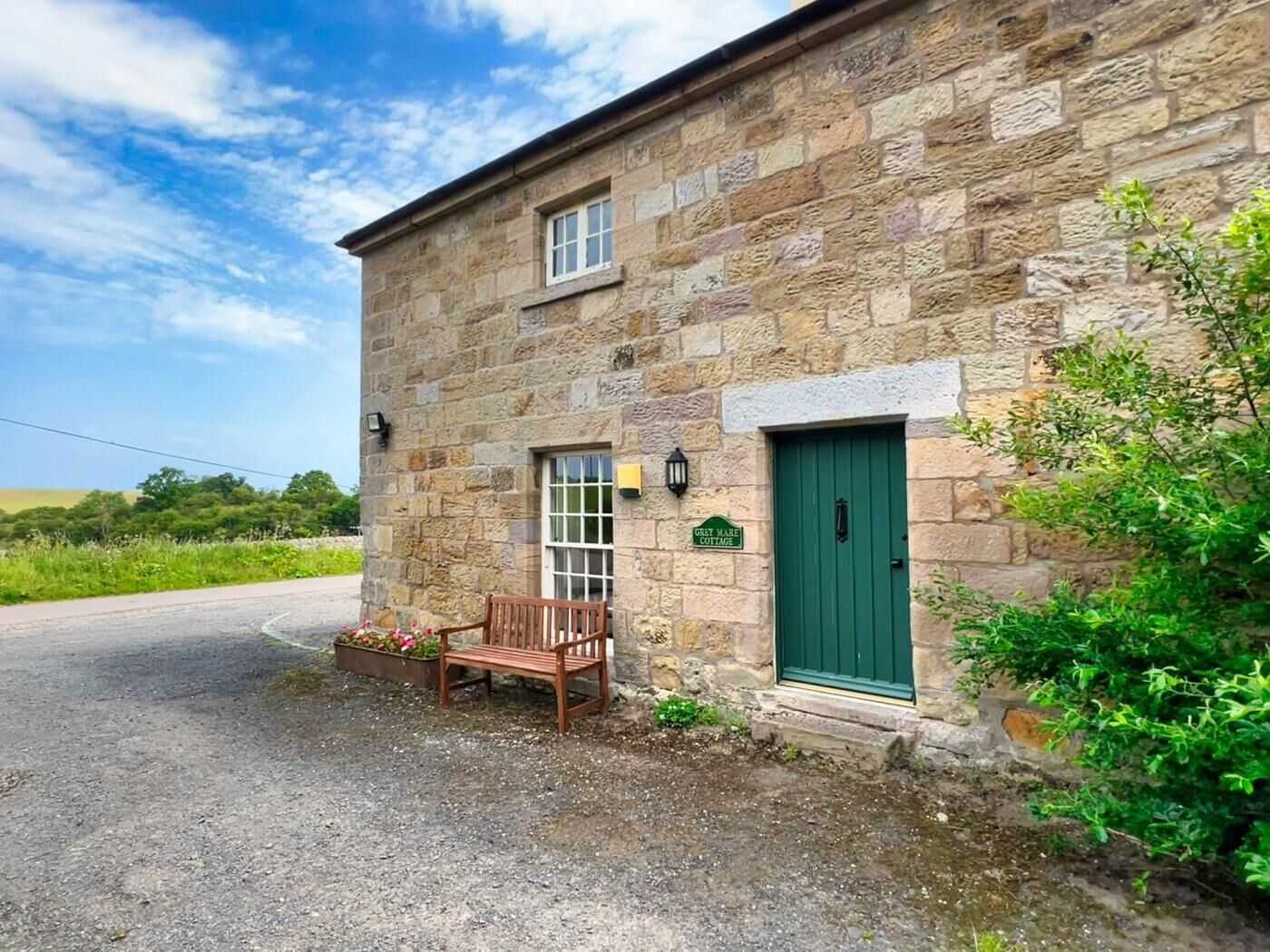 Ein Steinhaus mit grüner Tür, einer Bank davor und einem Schild, auf dem 'Grey Mare Cottage' steht.