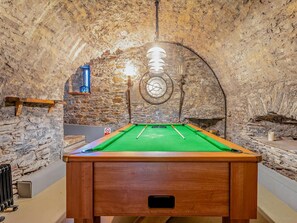 A pool table in a room with stone walls and a clock.