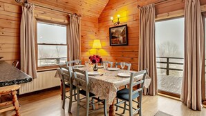 Un coin repas avec une table dressée pour six personnes, des murs en bois, un lustre et un tableau accroché au mur.