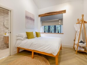 Une chambre à coucher comprenant un lit, une fenêtre, une tête de lit en bois, une œuvre d’art accrochée au mur et un porte-serviettes en bois.
