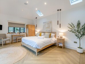 Ein modernes Schlafzimmer mit einem großen Bett, einem Schreibtisch und einem Stuhl. Eine Topfpflanze und ein an der Wand befestigter Fernseher sind ebenfalls vorhanden.