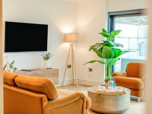 Ein Wohnzimmer mit Sofa, Couchtisch, Fernseher, Lampe und einem Fenster mit Blick.
