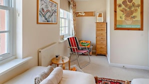 Ein Schlafzimmer mit Bett, Stuhl, Kommode, Heizkörper, Fenster und Bildern an den Wänden.
