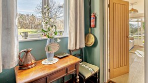 A room with a wooden table, a vase with flowers, a metal pitcher, a fire extinguisher, and a door leading outside. - 2 Bed in Grange-over-sands (oc-95811) (Crosthwaite and Lyth)