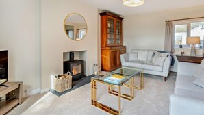 A living room with a fireplace, a sofa, a glass coffee table, a television, and a wooden cabinet. - 2 Bed in Grange-over-sands (oc-95811) (Crosthwaite and Lyth)
