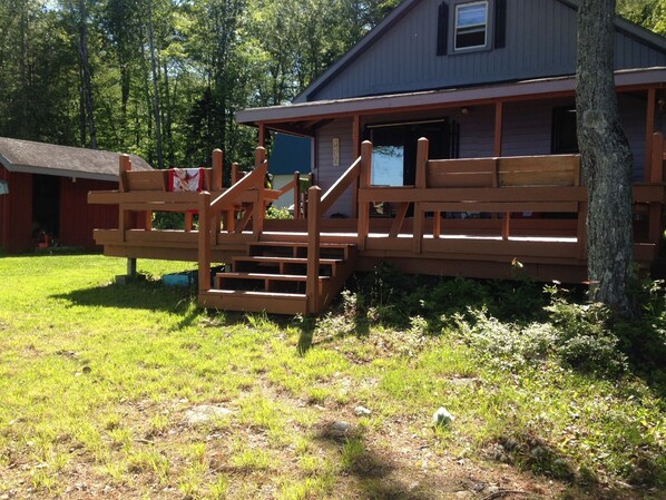 A wooden deck with a staircase leading to a building with a window and a door. - Cozy 2-bedroom cabin on beautiful crystal clear Schoodic Lake (Brownville)