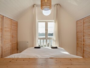 A bedroom with a large bed, a window with curtains, and wooden paneling on the walls.