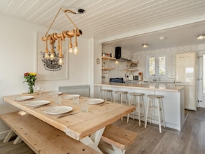 A dining area with a wooden table set for four, a hanging light fixture, and a kitchen with a herringbone pattern backsplash and a vintage-style refrigerator.