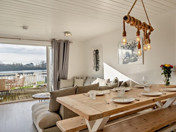 Un comedor con una mesa de madera dispuesta para cuatro personas, un sofá y vista a un lago.