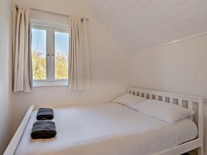Una cama individual con ropa blanca y dos toallas oscuras sobre un marco blanco.