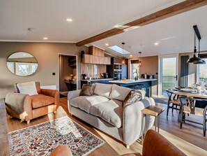 A modern living room with a sofa, a dining table, and a kitchen in the background.