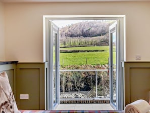 A room with a large window offering a view of a green field and a hill.