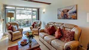 A living room with a sofa, two armchairs, a coffee table with flowers, and a painting of a bull. - 2 Bed in Llanidloes (oc-95815) (Llanidloes Without)