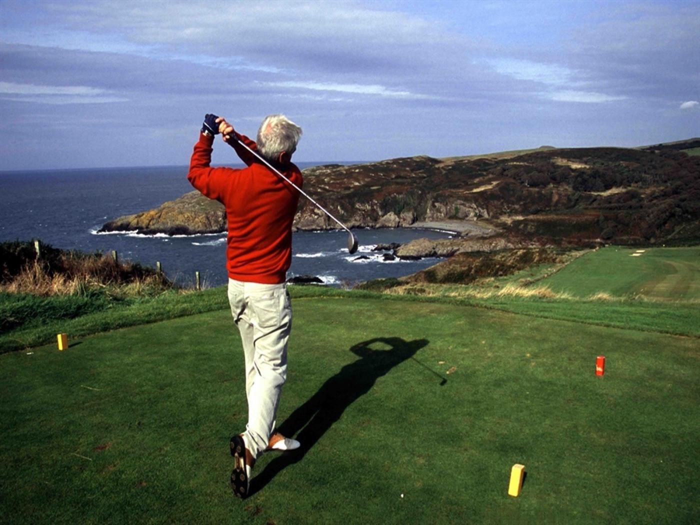 A person playing golf on a green with a view of the ocean and hills in the background.