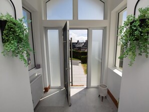 Ein Flur mit Glastür zum Außenbereich, einem Heizkörper und einem kleinen Hocker.