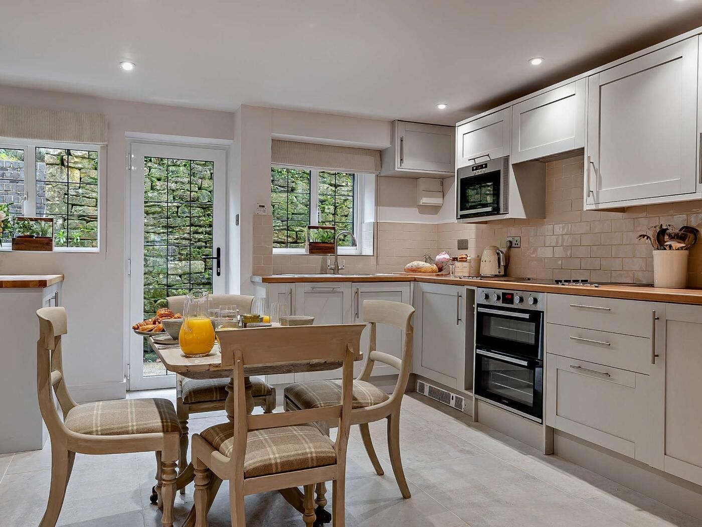 A modern kitchen with a dining area, featuring a large window, a microwave, an oven, and a dining table with chairs.