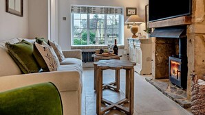 Een gezellige woonkamer met een open haard, een bank, een tafel en een raam met uitzicht op het omliggende landschap.